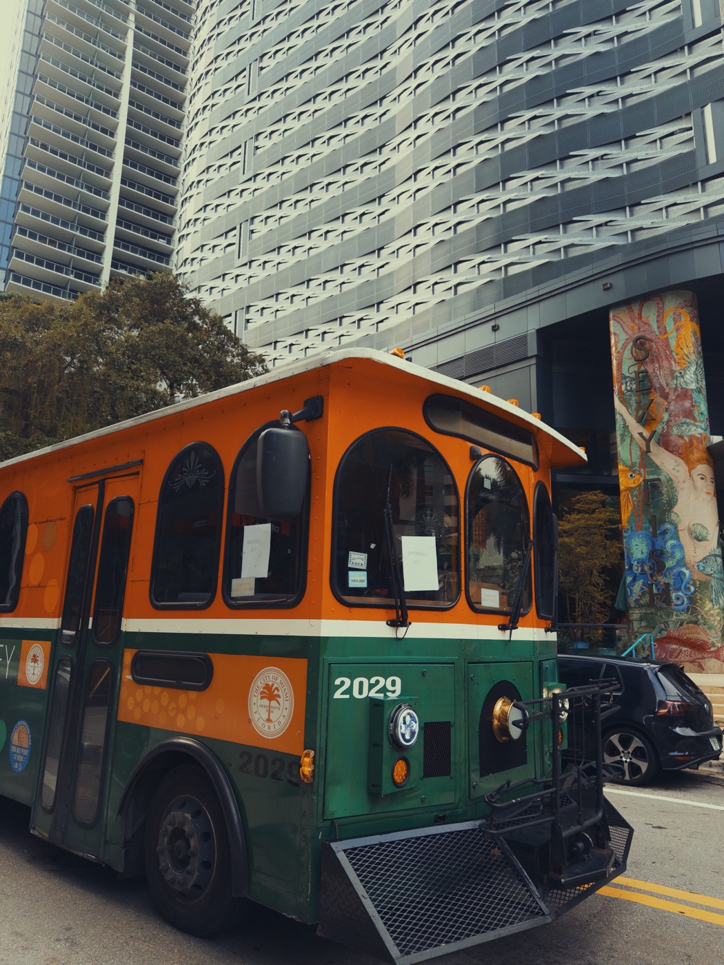 An orange and green trolley under glass towers